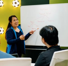 a person pointing at a whiteboard with a person sitting in front of her