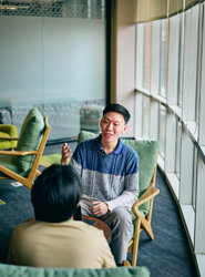 a man sitting in a chair talking to another man