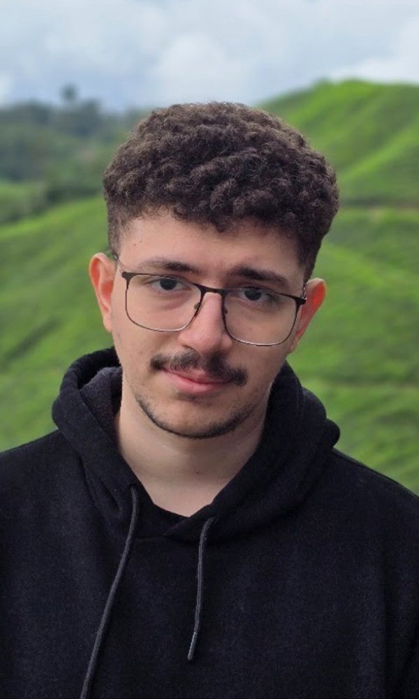 a person with glasses and a mustache in front of a green hill