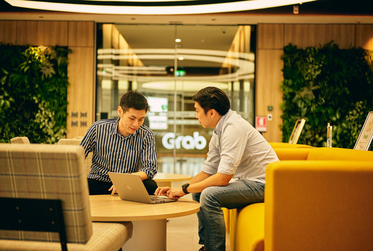 two men sitting at a table looking at a laptop