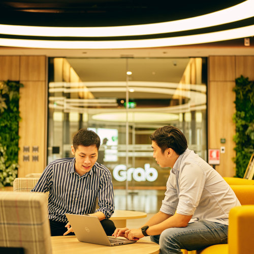 two men sitting at a table looking at a laptop